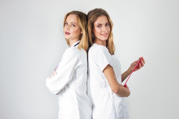 Dos doctores muy jóvenes de las mujeres, enfermeras que se colocan de nuevo a la parte posterior en el hospital.