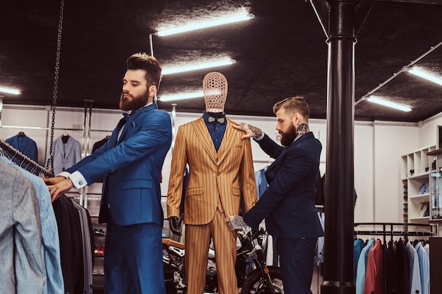 Dos elegantes asistentes de tienda elegantemente vestidos que trabajan en una tienda de ropa masculina.