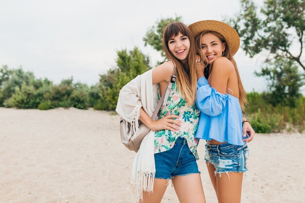 Dos elegantes mujeres muy sonrientes en vacaciones de verano en la playa tropical, amigos viajan juntos