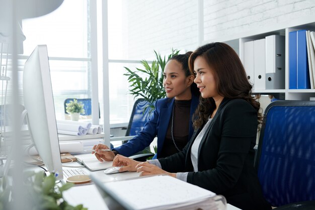 Dos empresarias asiáticas sentados juntos en la oficina en el escritorio y mirando la pantalla de la computadora