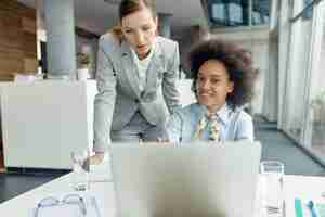 Foto gratuita dos empresarias cooperando mientras trabajan en una laptop en la oficina