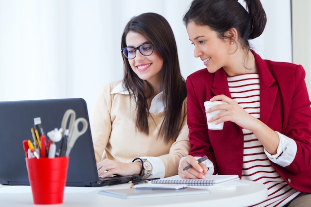 Foto gratuita dos empresarias jovenes que trabajan con la computadora portátil en su oficina.