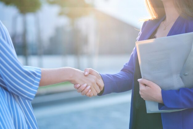 Dos empresarias ocupadas tienen una reunión informal afuera, se saludan con un apretón de manos.