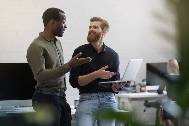 Dos empresarios alegres discutiendo algo en la computadora portátil y sonriendo