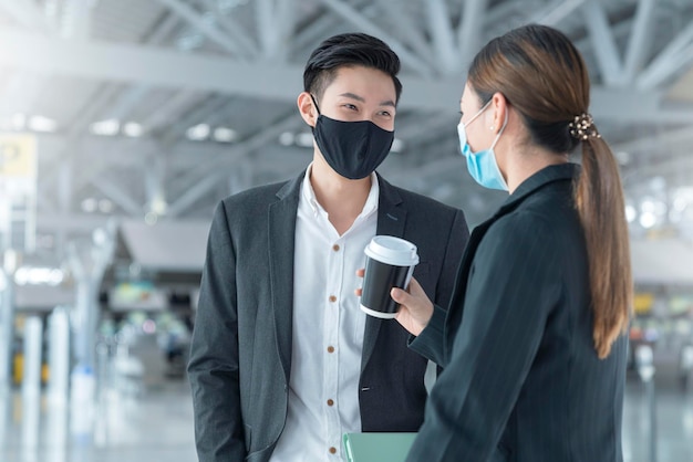 Dos empresarios y empresarias asiáticos con protección de mascarilla en la terminal del aeropuerto internacional reunión de tableta conversación cerca del área del banco de espera nuevo concepto de negocio de viajes normal