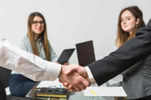 Foto gratuita dos empresarios estrecharme la mano delante de ejecutivo femenino en el lugar de trabajo