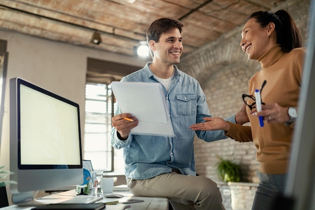 Foto gratuita dos empresarios felices analizando informes comerciales y comunicándose en la oficina