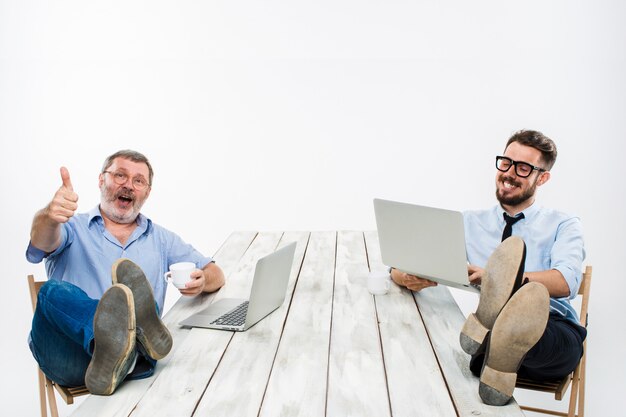 Los dos empresarios con patas sobre la mesa trabajando en computadoras portátiles