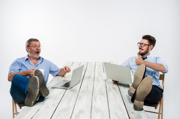 Los dos empresarios sonrientes con las piernas sobre la mesa trabajando en portátiles sobre fondo blanco. Negocios al estilo americano