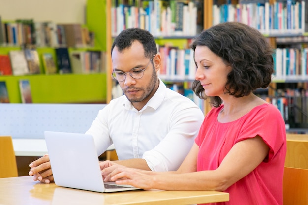 Dos estudiantes adultos colaborando en proyecto en biblioteca