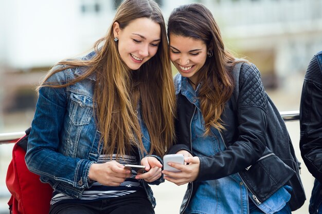 Dos estudiantes hermosos que usan el teléfono móvil en la calle.