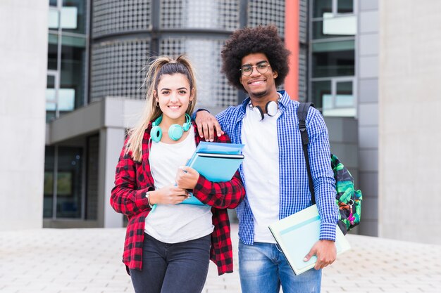 Dos estudiantes jóvenes felices mirando a la cámara de pie frente al edificio de la universidad