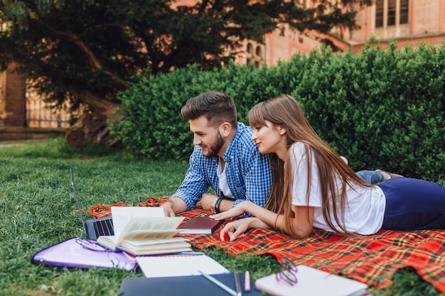 Dos estudiantes se sientan en el campus de césped y trabajan en una computadora portátil. Hermosa chica y chico guapo en la Universidad