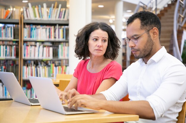 Dos estudiantes universitarios adultos que trabajan en la clase de informática de la biblioteca