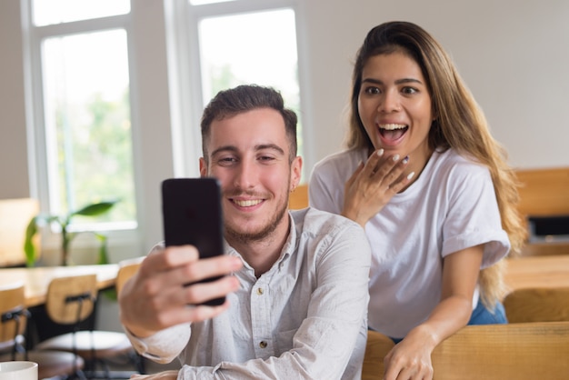 Dos felices estudiantes masculinos y femeninos de videoconferencia en café