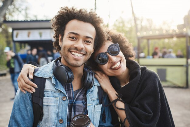 Dos felices viajeros afroamericanos con peinado afro abrazándose y mirando a cámara, haciendo fotos mientras caminan en el parque, expresando emociones positivas.