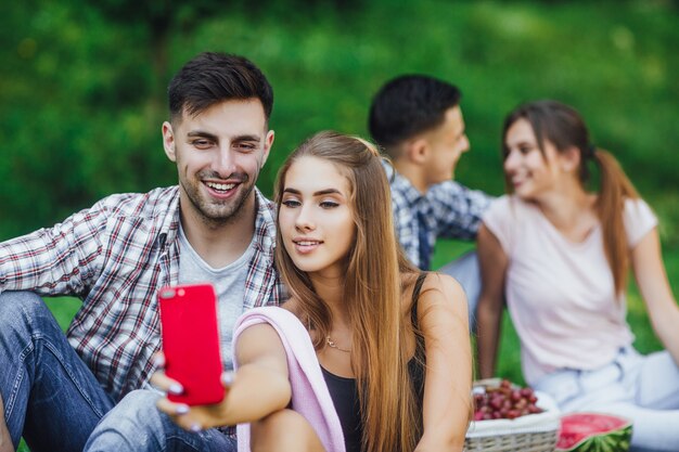 Dos feliz pareja de jóvenes sentados en la hierba en el hermoso parque, tienen un picnic