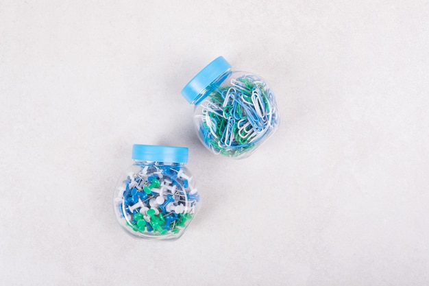 Dos frascos azules llenos de alfileres de colores y clips de papel sobre fondo beige. Foto de alta calidad