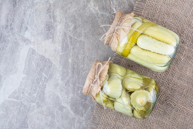 Dos frascos de diversas verduras encurtidas sobre arpillera.