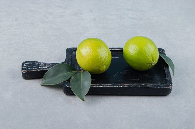 Dos frutos de limón con hojas en la tabla de cortar.