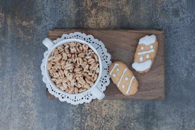 Dos galletas de Navidad y un tazón de cacahuetes dulces sobre tabla de madera. Foto de alta calidad