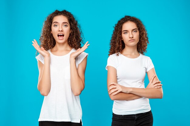 Dos gemelos de mujer joven posando sobre azul.