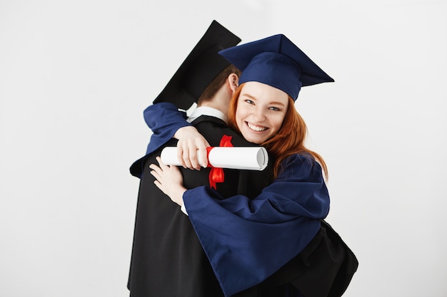 Dos graduados abrazando sobre superficie blanca Ginger mujer sonriendo