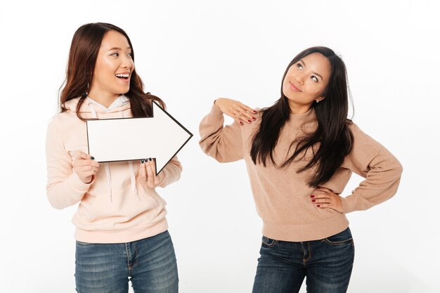 Dos hermanas asiáticas positivas damas sosteniendo flecha.