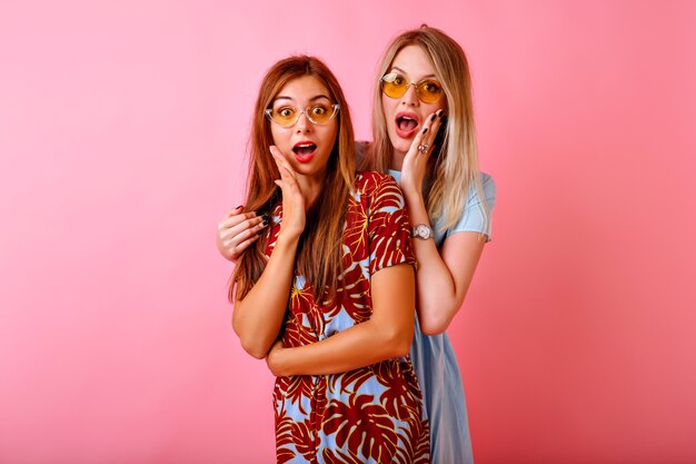 Dos hermanas bonitas felices mejores amigos hipster mujeres divirtiéndose juntos en el fondo de estudio rosa