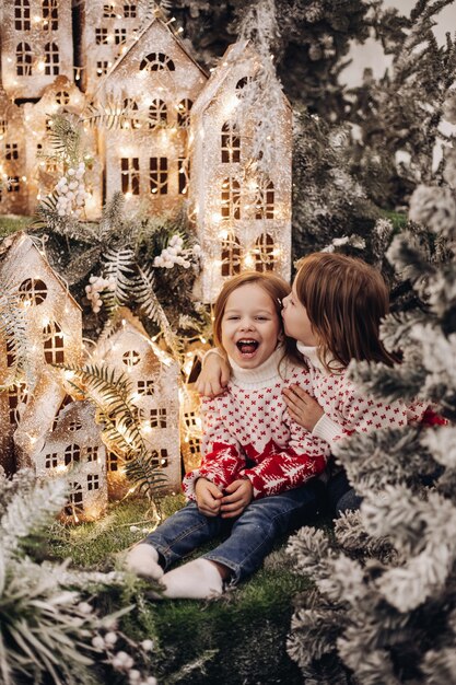 Dos hermanas caucásicas posa para la cámara en una hermosa decoración navideña con muchos árboles y nieve en el fondo