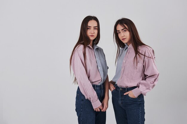 Dos hermanas gemelas de pie y posando en el estudio con fondo blanco.