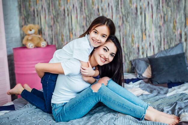 Dos hermanas lindas felices acostado en la cama en el dormitorio en casa y jugando