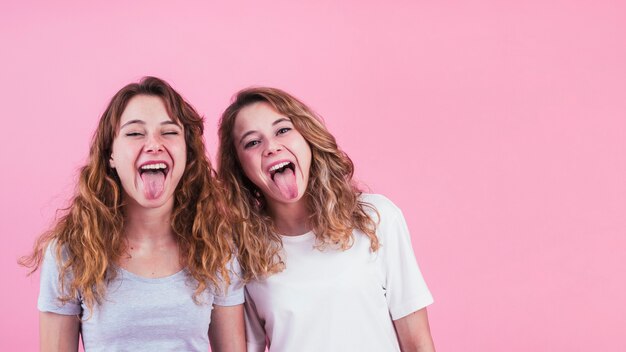 Dos hermanas mostrando su lengua contra el fondo rosa