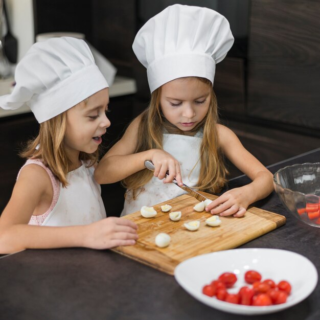 Dos hermanas en el sombrero del cocinero y el delantal que cortan los huevos hervidos en tajadera de madera