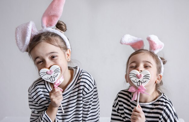 Dos hermanitas divertidas están posando con pan de jengibre de Pascua en forma de caras de conejito.