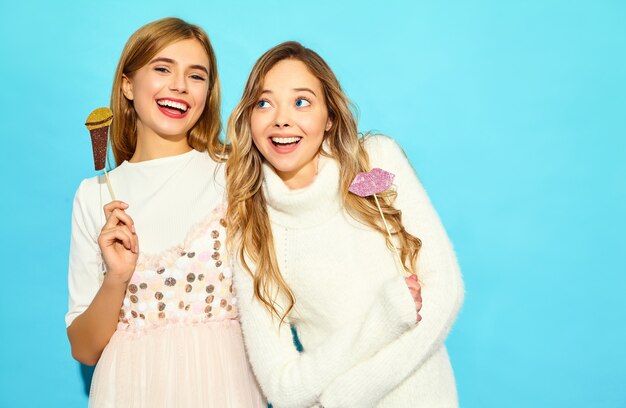 Dos hermosa joven cantando con accesorios de micrófono falso. Mujeres de moda en ropa casual de verano. Modelos divertidos aislados en la pared azul