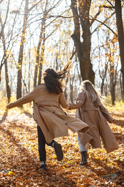 Dos hermosas amigas pasando tiempo juntas. Dos jóvenes hermanas sonrientes caminando en el parque de otoño. Chicas morenas y rubias con abrigos.