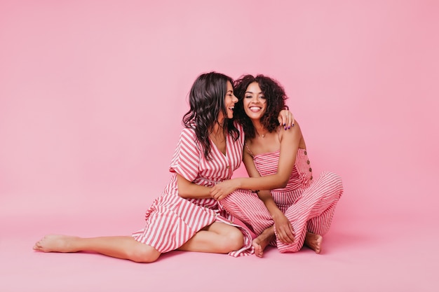 dos hermosas chicas de cabello oscuro con hermosas sonrisas bronceadas y brillantes, vestidas con pijamas a rayas posan y se divierten