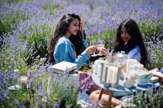 Dos hermosas chicas indias sentadas en un campo de lavanda púrpura con decoración con gafas en las manos