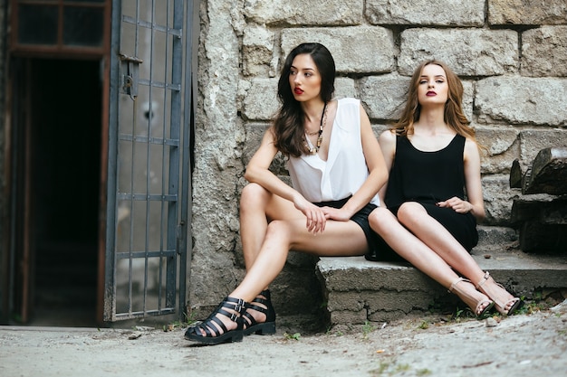 Dos hermosas chicas jóvenes posando en contra de un edificio abandonado