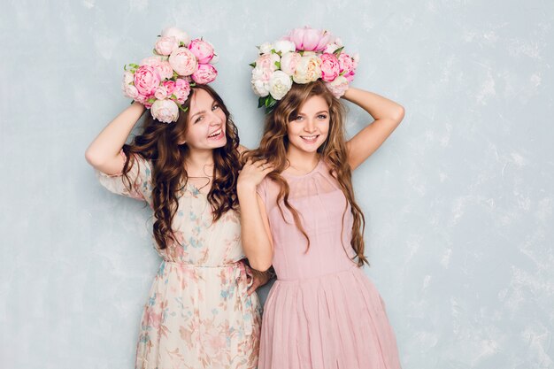 Dos hermosas chicas se paran en un estudio, hacen el tonto y tienen círculos de flores en la cabeza.