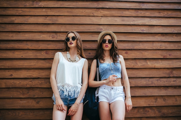 Dos hermosas chicas posan frente a una pared de madera