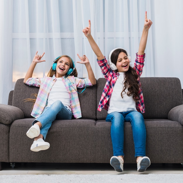 Dos hermosas chicas relajadas disfrutando de la música en los auriculares levantando sus manos bailando