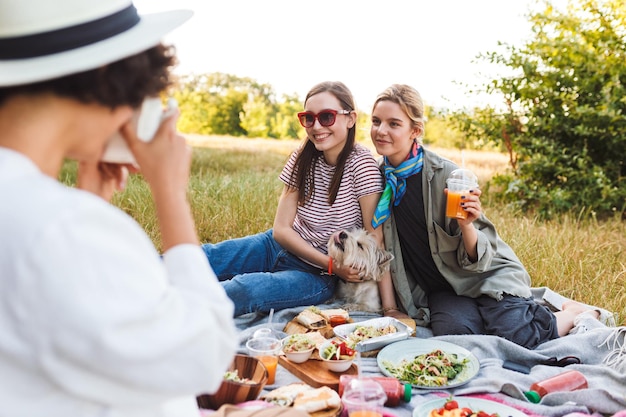 Dos hermosas chicas sentadas con un perrito en una manta de picnic y posando en la cámara felizmente pasando tiempo en un picnic en el parque