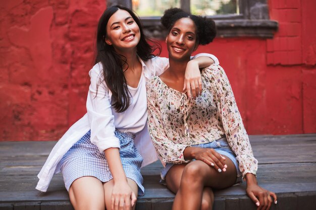 Dos hermosas chicas sonrientes mirando felizmente a la cámara mientras pasan tiempo juntas en un acogedor patio