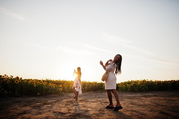 Dos hermosas jóvenes amigas negras usan pose de vestido de verano en un campo de girasoles