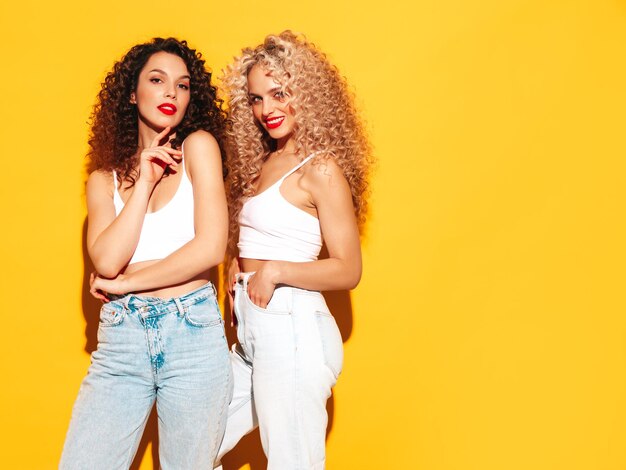 Dos hermosas mujeres hipster sonrientes sexy en ropa de verano Modelos de moda con peinado de rizos afro divirtiéndose en el estudio Mujer caliente aislada en amarillo