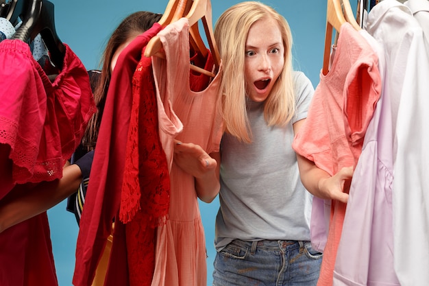 Las dos hermosas mujeres jóvenes que miran vestidos y se lo prueban mientras eligen en la tienda