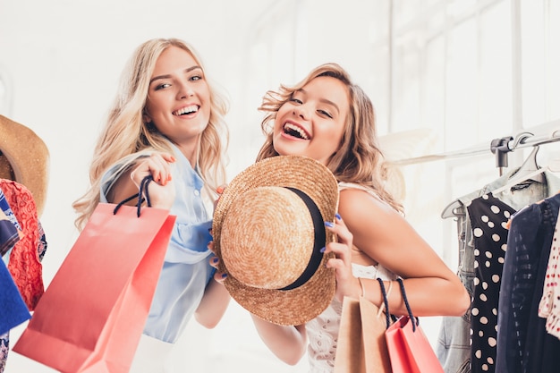 Las dos hermosas mujeres jóvenes que miran vestidos y se lo prueban mientras eligen en la tienda