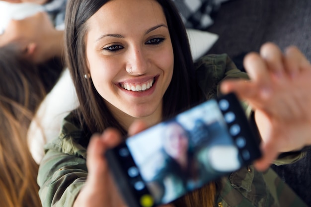 Dos hermosas mujeres jóvenes utilizando teléfono móvil en casa.